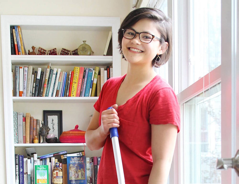 A smiling Two Bettys Green Cleaning cleaner wearing a red shirt in front of a bookcase