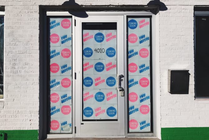 The front door of Two Bettys Refill Station, which is papered with Two Bettys logos and "coming soon" posters