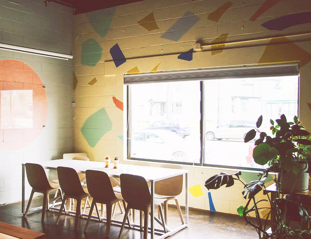 A long white table with eight chairs surrounding it in an office with a large window.