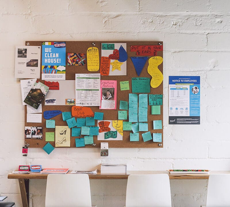 A bulletin board at Two Bettys Refill Station covered in colorful notes and posters