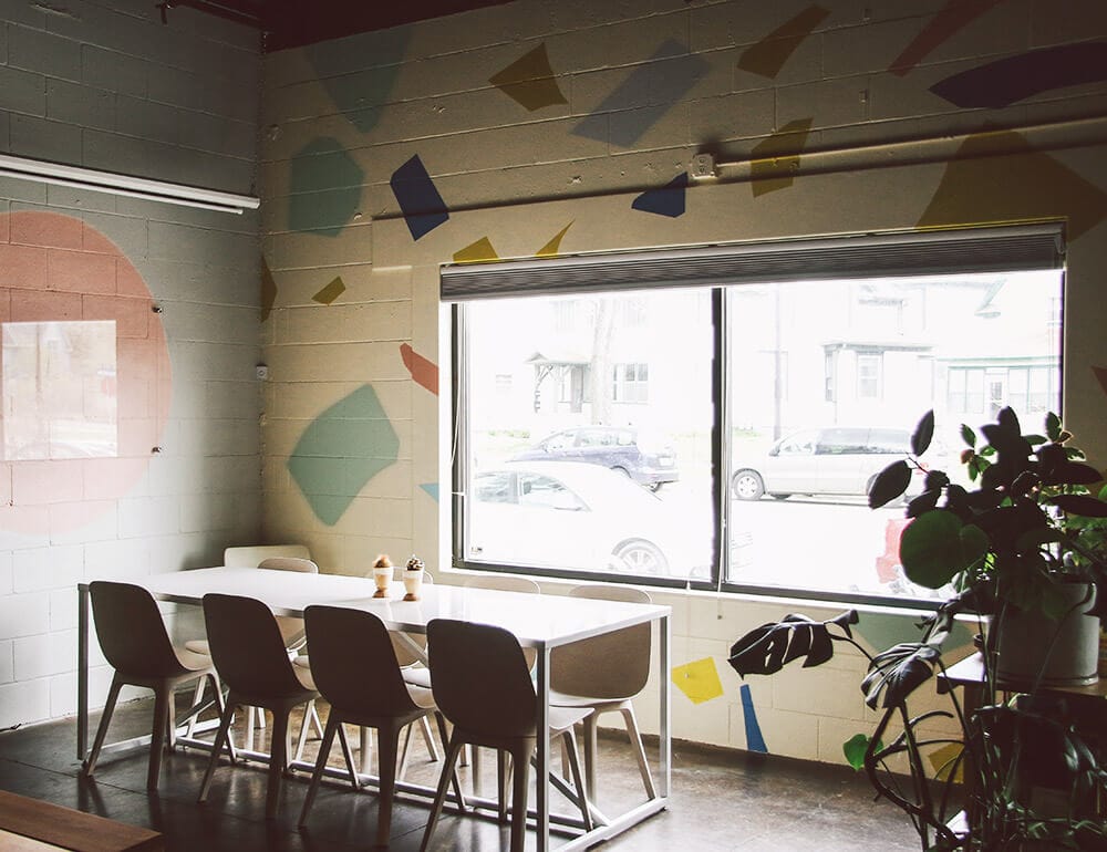 A long white table with eight chairs surrounding it in an office with a large window.