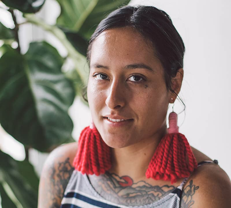 A latinx woman wearing large red yarn earrings smiling at the camera.