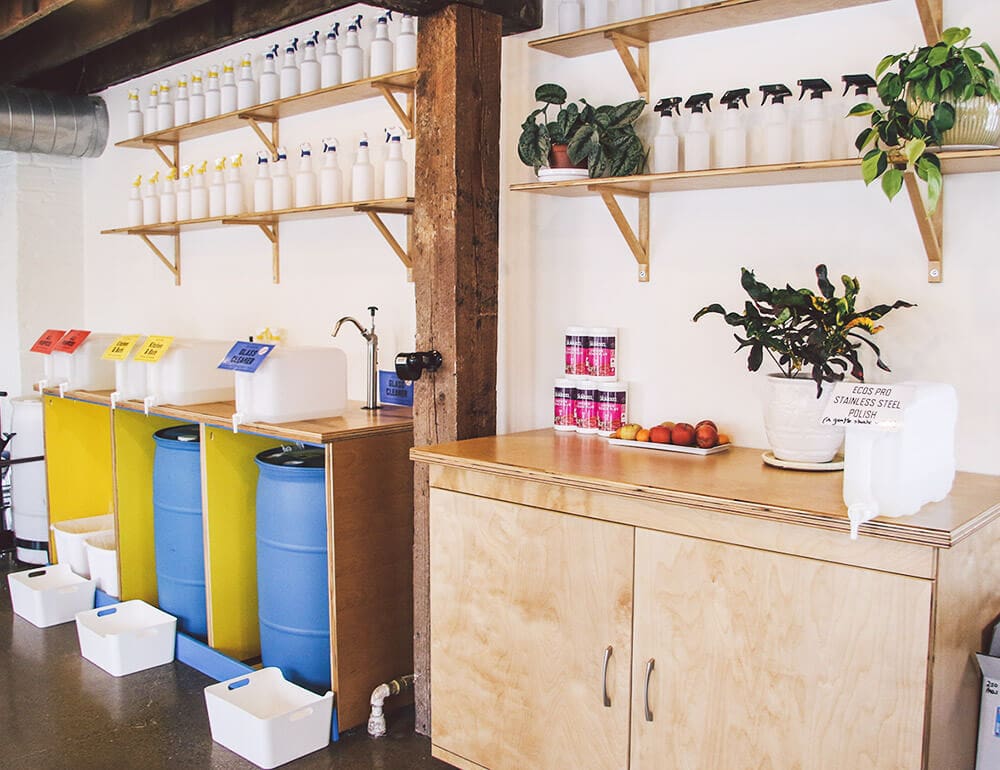 Inside Two Bettys Refill Station, featuring large blue barrels and white spray bottles.