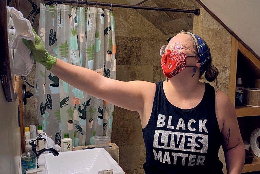 A person wearing a red mask and Black Lives Matter tank top cleaning a residential bathroom.