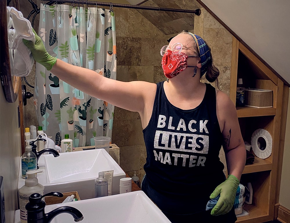 A person wearing a red mask and Black Lives Matter tank top cleaning a residential bathroom.
