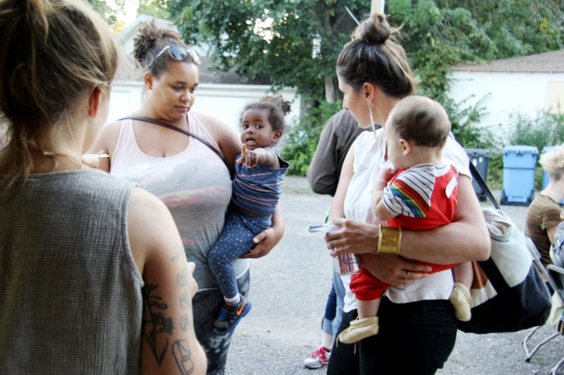 Two women in conversation, holding babies on their hips