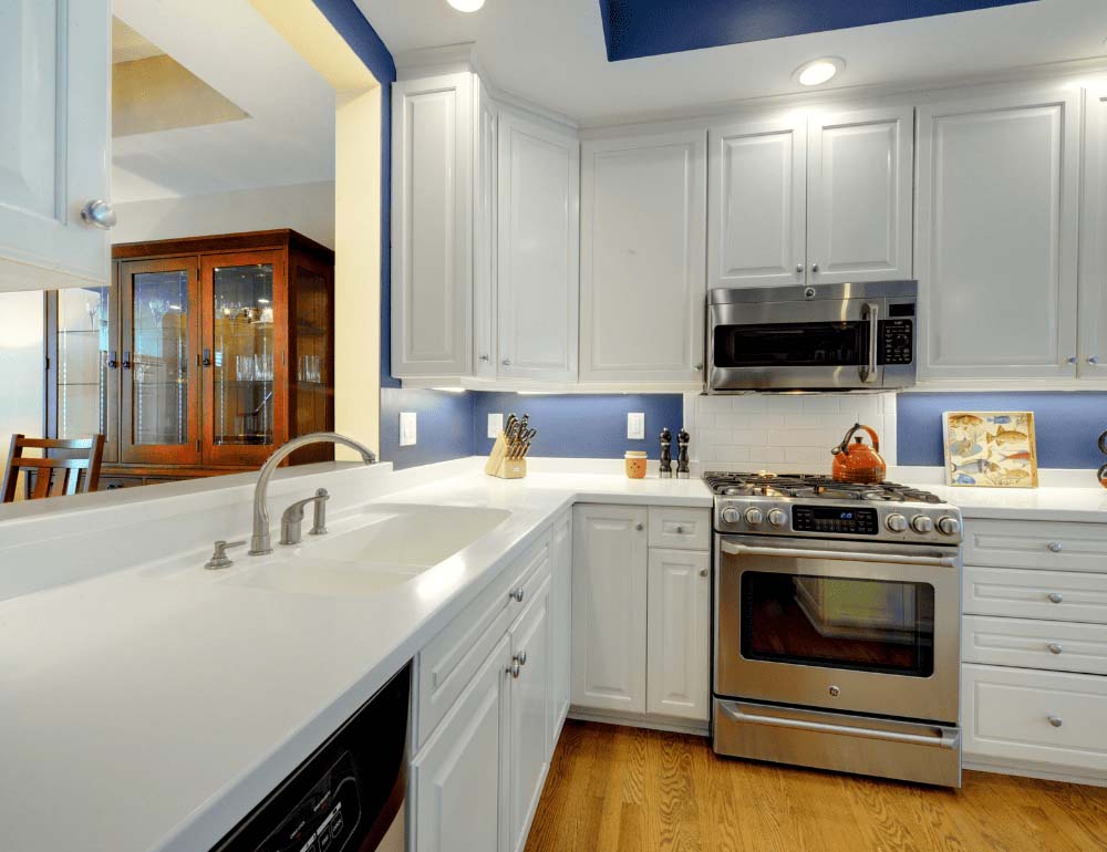 A bright and clean kitchen with white cabinets and counters and dark blue walls.