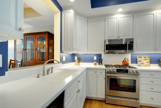 A bright and clean kitchen with white cabinets and counters and dark blue walls.