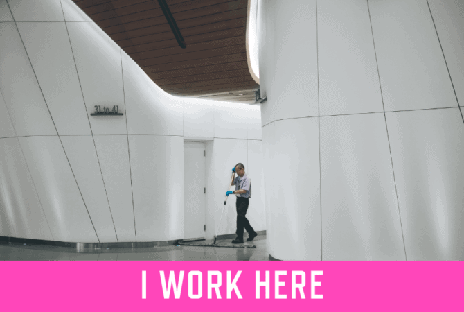 A janitor cleaning the floors in a modern office building, with the text "I WORK HERE" underneath. Photo by Verne Ho